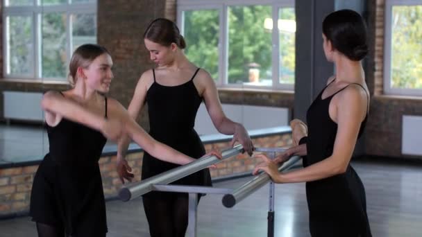 Vidám balerinák beszélgetnek bemelegítés közben a Barre-ban — Stock videók