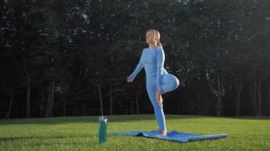 Sarışın kadın güneşli park çimlerinde yoga yapıyor.
