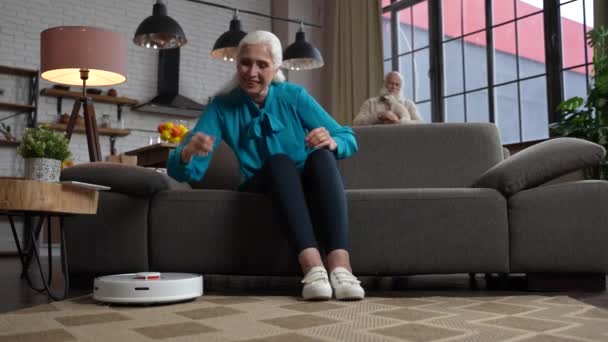 Gelukkig verouderde vrouw zet robot stofzuiger — Stockvideo