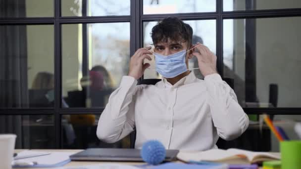 Серьезный индийский мужчина в маске для лица позирует в офисе — стоковое видео
