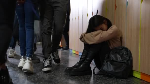 Расстроенная азиатская школьница сидит на полу в школе — стоковое видео