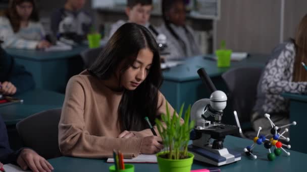 Smiling asian schoolgirl posing on camera at desk — Stok Video