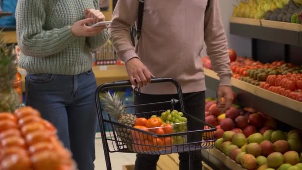 Jong stel vullende winkelwagen in supermarkt — Stockvideo