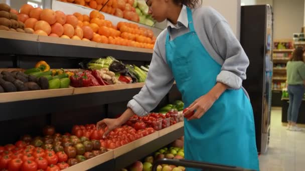 Жінка-працівник кладе помідори на підставку в магазині — стокове відео