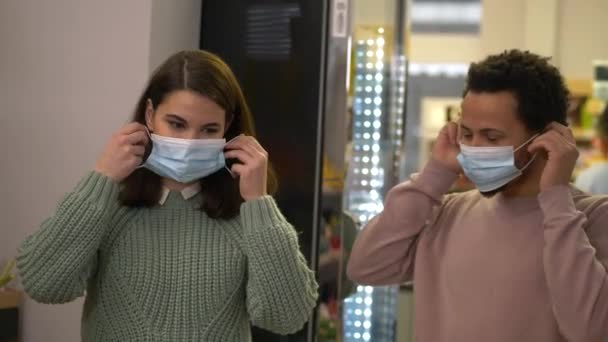 Мультинациональная пара надевает маски в супермаркете — стоковое видео