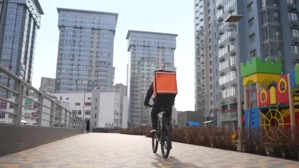 Entrega de comida hombre montar en bicicleta a lo largo del camino del patio — Vídeo de stock