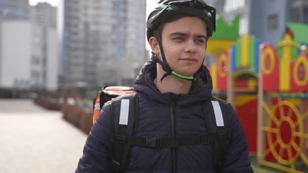 Man food courier with bike walking past playground — Stock Video