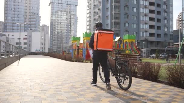 Correio de comida andando com saco térmico e bicicleta — Vídeo de Stock