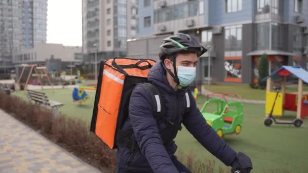 Levering koerier paardrijden fiets langs stedelijke speeltuin — Stockvideo