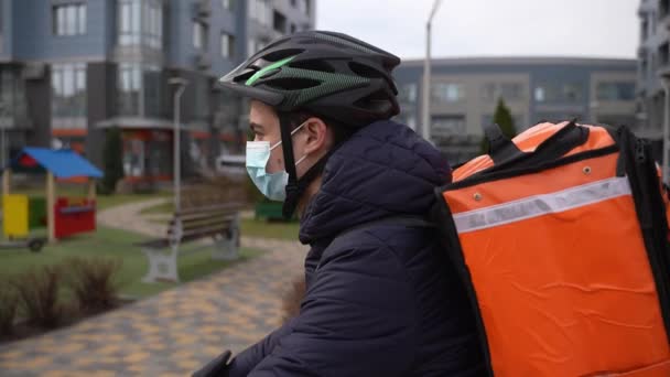 Lebensmittelkurier mit Gesichtsmaske radelt durch die Stadt — Stockvideo