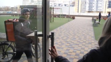 Kadın müşteri ön kapıdan pizza getiriyor.