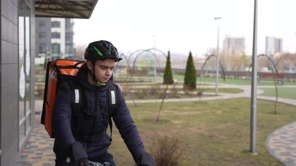 Comida mensajero montar en bicicleta y entrar en el edificio — Vídeos de Stock