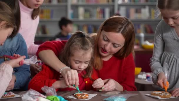 Женщина помогает аутичной девочке глазурью печенье в классе — стоковое видео