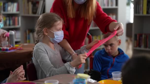 Sınıfta balçık geren maskeli öğretmen ve kız. — Stok video