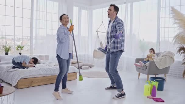 Padres alegres bailando con dispositivos de limpieza — Vídeo de stock