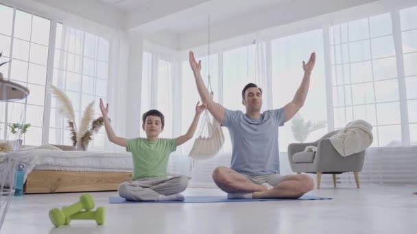 儿子在家里做瑜伽的男人坐在垫子上 — 图库视频影像