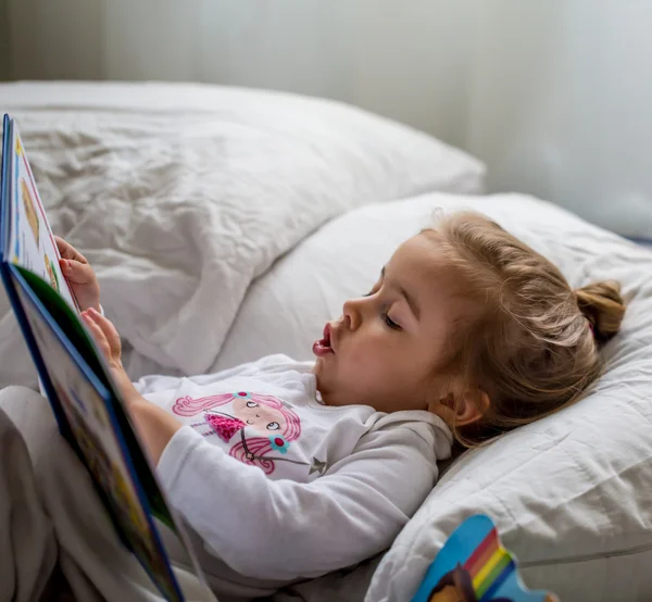 Niña lee un libro infantil en la cama después de dormir —  Fotos de Stock