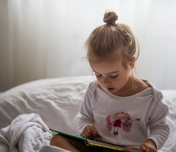 Маленькая девочка читает детскую книгу в постели после сна — стоковое фото