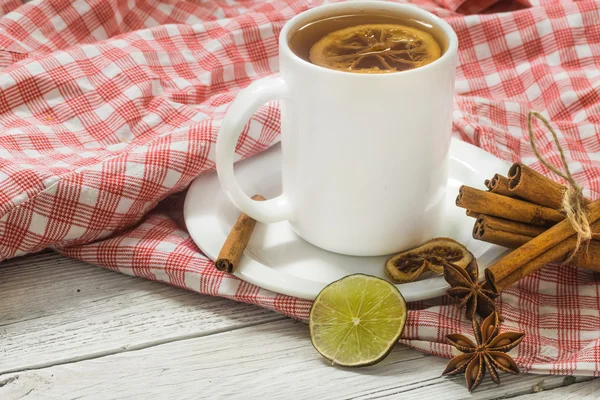 Xícara de chá em uma toalha de mesa vermelha, belo fundo de madeira branco, paus de canela, limão e bagas — Fotografia de Stock