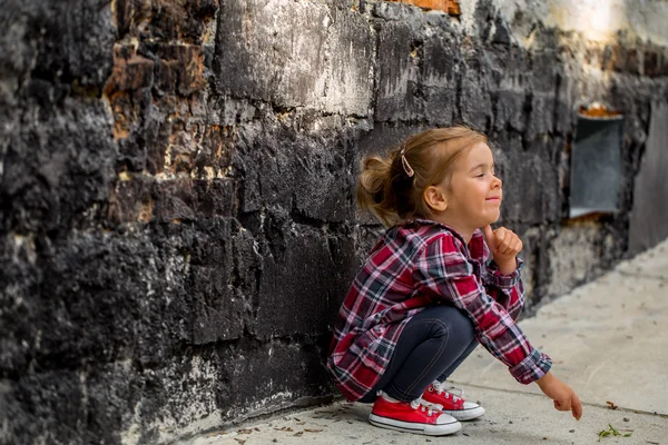 Маленькая красивая девочка у стены брик — стоковое фото