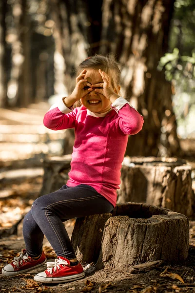 Красивая маленькая девочка сидит на пне в лесу — стоковое фото