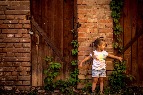 Красивая маленькая девочка играет возле заброшенных зданий и старых дверей — стоковое фото