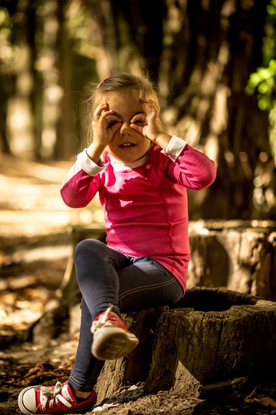 Linda menina sentada em um toco na floresta — Fotografia de Stock