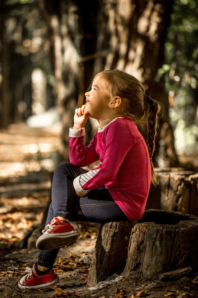 Linda menina sentada em um toco na floresta — Fotografia de Stock