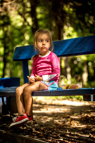 Красивая маленькая девочка сидит на скамейке в парке летний день — стоковое фото
