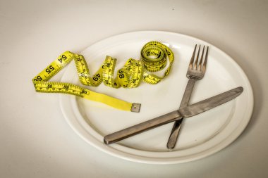 arka plan beyaz tabakta topuz, sarı şerit metre ve çatal bıçak takımı