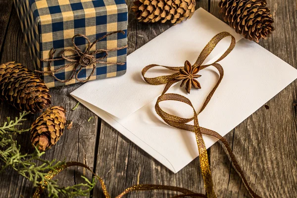 Білий конверт на дерев'яному фоні з сосновими шишками та різдвяним подарунком — стокове фото