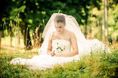 Orman yeşil bir çayırda oturan güzel genç gelin