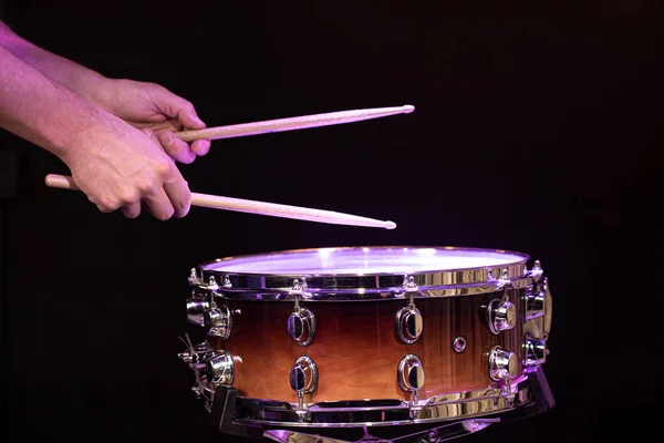 Drummer playing drum sticks on a snare drum on black background close up.