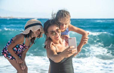 Çocuklu bir anne, deniz ve deniz dalgalarının arka planına selfie çeker. Aile ve eğlence kavramı.