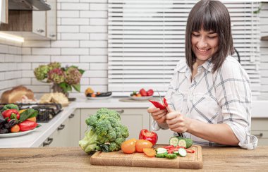 Neşeli esmer kız modern mutfağın arka planında sebze doğruyor..