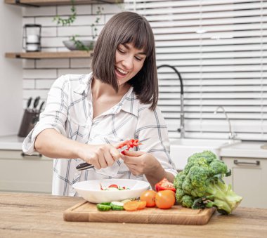 Mutfağın bulanık arka planında gülümseyen ve salata hazırlayan güzel esmer kadın..