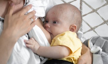 Annem yeni doğmuş bebeğini beyaz bir hamak sandalyesinde hafif bir arka planda emziriyor. Emzirme konsepti, kapat..