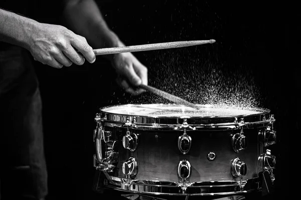 Drum sticks hitting snare drum with splashing water on black background under studio lighting. Black and white. Photo in motion.