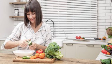 Neşeli esmer kız modern mutfağın arka planında sebze doğruyor..