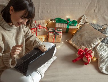 Rahat bir kazak giyen genç bir kadın internetten Noel hediyeleri alır. Çevrimiçi hediye seçme ve uzaklık verme kavramı.