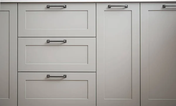 White kitchen cabinets with metal pulls or knobs on the doors close up.