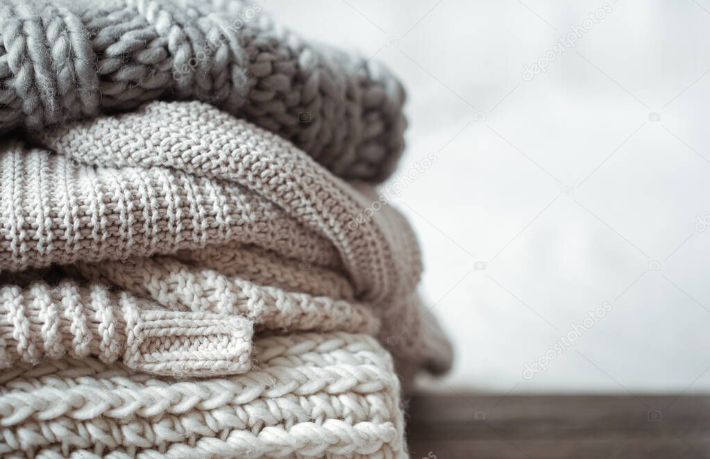 Close up of neatly folded knitted items of pastel color on a light background.