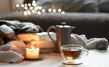 Bir fincan çay, bir çaydanlık, kitaplar ve yanan bir mumla dolu bulanık bir arka planda Bokeh ile..