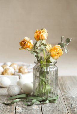 Cam bir vazoda bir buket çiçek. Arkaplanı bulanık dekoratif elementlerle dolu. Paskalya tatili konsepti.