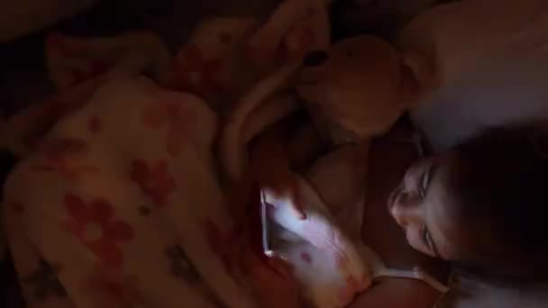 Uma Menina Deita Cama Com Brinquedo Macio Usa Smartphone Vez — Vídeo de Stock