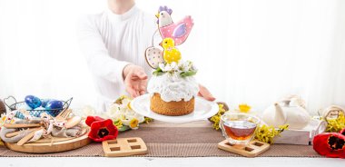 Kadınların elleri, çiçeklerle süslenmiş ve parlak detaylarla süslenmiş neşeli bir Paskalya pastası tutuyor..