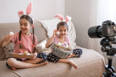 Paskalya yumurtalarıyla kameraya poz veren tavşan kulaklı küçük kardeşler. Paskalya fotoğraf oturumu konsepti.