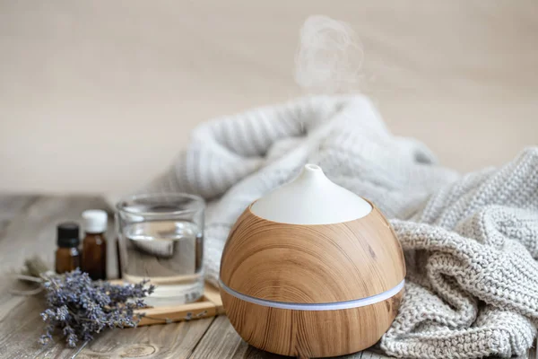 Modern aroma oil diffuser on wood surface with knitted element, water and lavender oil.