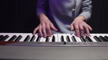 Karanlık bir arka planda piyano çalan bir kadının yakın çekimi. Pratik konsepti, müzik kaydı, performans.