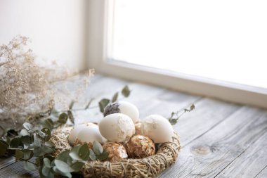 Paskalya, süslü Paskalya yumurtaları ve kuru dallarla dolu tahta bir yüzey üzerindeki dekoratif yuvalarla dolu..